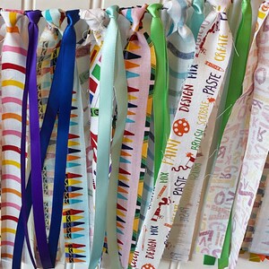 May include: A colorful fabric banner with the words "Design Mix", "Art Paste", "Brush", "Scribble", "Paste", and "Create" printed on it. The banner is decorated with colorful ribbons.