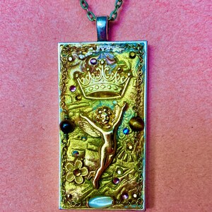 K&ouml;nnte beinhalten: Eine rechteckige Anh&auml;nger-Halskette mit einem goldfarbenen Engel, einer Krone und einem floralen Design. Der Anh&auml;nger ist mit bunten Edelsteinen und einer gr&uuml;nen Kette verziert. Der Hintergrund ist strukturiert gold und gr&uuml;n.