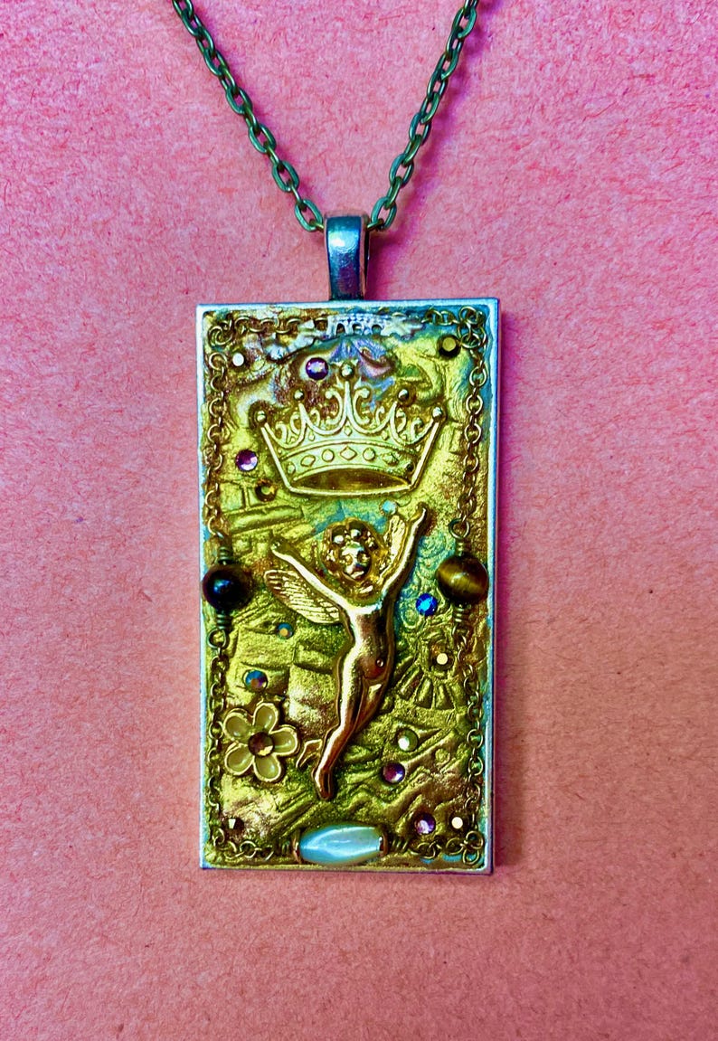 K&ouml;nnte beinhalten: Eine rechteckige Anh&auml;nger-Halskette mit einem goldfarbenen Engel, einer Krone und einem floralen Design. Der Anh&auml;nger ist mit bunten Edelsteinen und einer gr&uuml;nen Kette verziert. Der Hintergrund ist strukturiert gold und gr&uuml;n.
