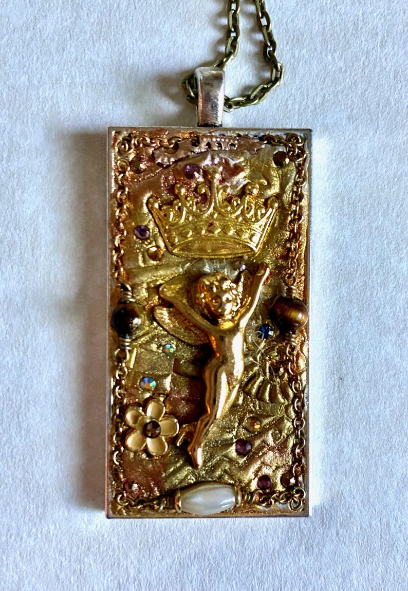 K&ouml;nnte beinhalten: Rechteckiger Anh&auml;nger mit goldfarbenem Rahmen und detailliertem Design. Der Anh&auml;nger zeigt eine goldene Krone, eine kleine Figur mit erhobenen Armen und verschiedene Verzierungen, darunter kleine Edelsteine und eine Blume. Er h&auml;ngt an einer filigranen Kette.