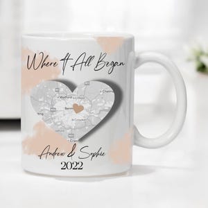 May include: White ceramic mug with a grey heart-shaped map design and the text "Where It All Began" and "Andrew & Sophie 2022".