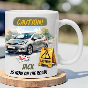 May include: A white ceramic mug with a black handle and the text "But First, Coffee" in a bold, black font. The mug is set against a blurred background, suggesting a cosy setting.