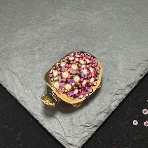 Pode incluir: Um broche de tartaruga dourado com um design de cristal rosa e branco.