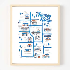 May include: A framed art print featuring a hand-drawn map of Phinney Ridge, with blue and orange illustrations of local businesses. The title "Phinney Ridge" is written in blue script. The print is in a light wood frame.