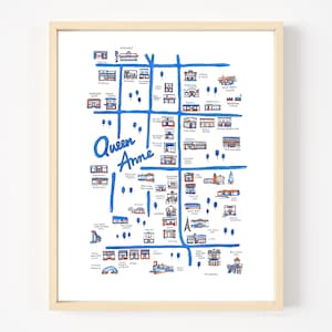 May include: A framed art print featuring a hand-drawn map of the Queen Anne neighborhood. The map uses blue lines for streets and orange and blue ink for various buildings, landmarks, and small trees, with the text Queen Anne written in blue.