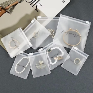 May include: A selection of clear plastic bags, each with a zip closure, containing jewellery. The bags are printed with "Peony sewing shop" in a cursive script. The jewellery includes rings, bracelets, and necklaces, visible through the transparent material.