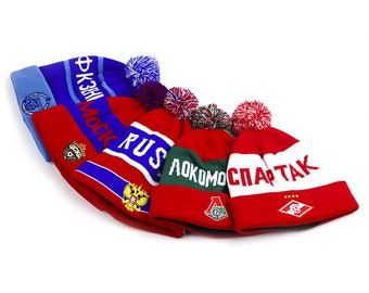 Può includere: Cinque berretti invernali a maglia con pon pon. I berretti sono rossi, blu, bianchi e verdi con vari loghi di squadra e testo, tra cui "SPARTAK", "LOKOMOTIV", "RUSSIA" e "FK ZNAMIYA TRUDA MOSKVA".