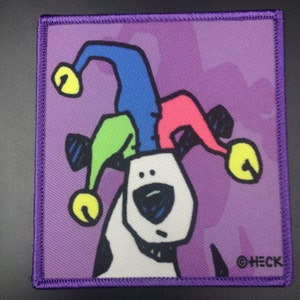 May include: A white dog with black spots wearing a multi-colored jester hat with bells. The hat is blue, green, pink, and yellow. The dog is looking to the left. The background is purple with a pattern. The image has the text "©HECK" in the bottom right corner.