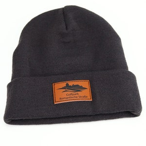 May include: A dark gray knit beanie with a brown leather patch that says "Golfpark Romantische Stra&szlig;e".