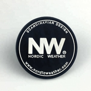 Puede incluir: Un parche circular de goma negra con texto blanco en relieve. El centro muestra las letras NW, con las palabras SCANDINAVIAN DESIGN, NORDIC WEATHER y el sitio web www.nordicweather.com impresos en un patrón circular en el borde.