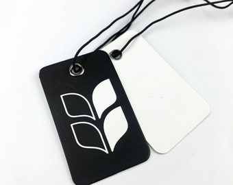 Pode incluir: Duas etiquetas retangulares com um cordão preto. Uma etiqueta é preta com um design de trigo estilizado branco. A outra etiqueta é branca. Ambas as etiquetas têm um ilhó de metal prateado.