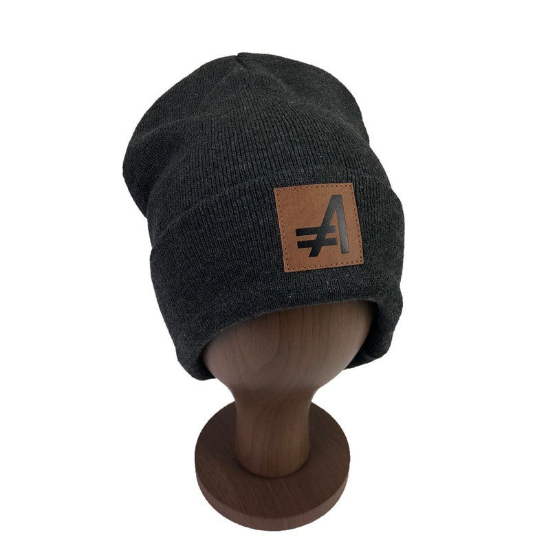May include: Gray knit beanie with a brown leather patch featuring a black stylized letter "A" with a line through it.
