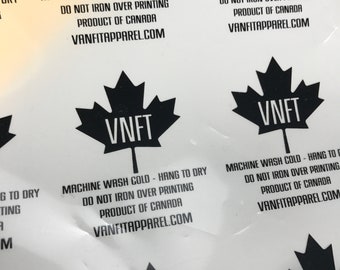May include: A white label with black text and a black Canadian maple leaf logo. The text reads "MACHINE WASH COLD - HANG TO DRY DO NOT IRON OVER PRINTING PRODUCT OF CANADA VANFITAPPAREL.COM" and the logo has the letters "VNFT" inside the maple leaf.