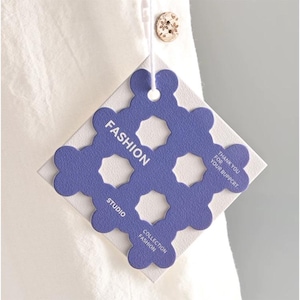 Könnte beinhalten: Ein quadratisches weißes Kleidungsetikett mit einer violetten, gestanzten Auflage in einem gewellten Gittermuster. Das Etikett zeigt den Text FASHION, STUDIO, COLLECTION FASHION und THANK YOU FOR YOUR BUPPCRT in weißer Schrift.