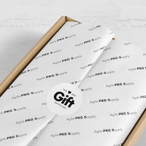May include: A brown cardboard box containing white tissue paper printed with the repeating black text Agile PKG Supply. A circular white sticker is centered on the tissue paper, featuring the black text Gift with a small heart icon above it.
