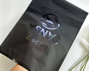 May include: Black plastic bag with a zipper closure. The bag has a logo that says "SANS" with "Est. 2022" below it. The logo is in a silver color and has a stylized "S" in a circle. The text "www.sans.vip.com" is printed on the top of the bag.