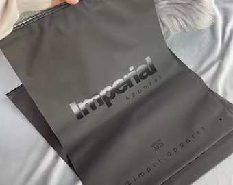 May include: Dark gray apparel packaging bag with the word "Imperial" in a metallic silver font. The word "Apparel" is below the word "Imperial". The text "since 2023" and "@imprl.apparel" are also visible.