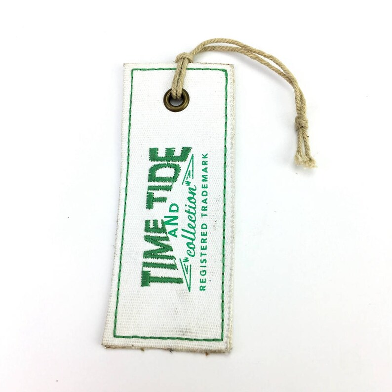 May include: White fabric tag with a green embroidered logo that says "Time and Tide Collection" and "Registered Trademark". The tag has a brown metal eyelet and a brown string attached.