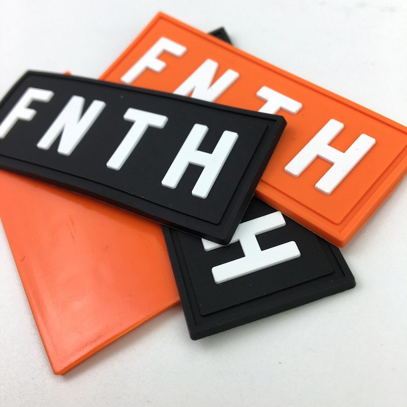 May include: Three black and orange fabric patches with white lettering. The patches spell out "FNTH" in different arrangements.