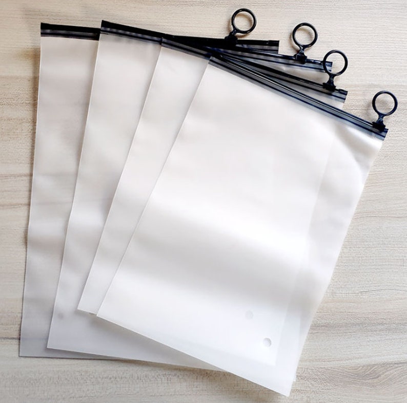 Pu&ograve; includere: Quattro sacchetti di plastica trasparenti con cerniera, tiretti neri e bordi neri. I sacchetti sono impilati uno sopra l'altro.