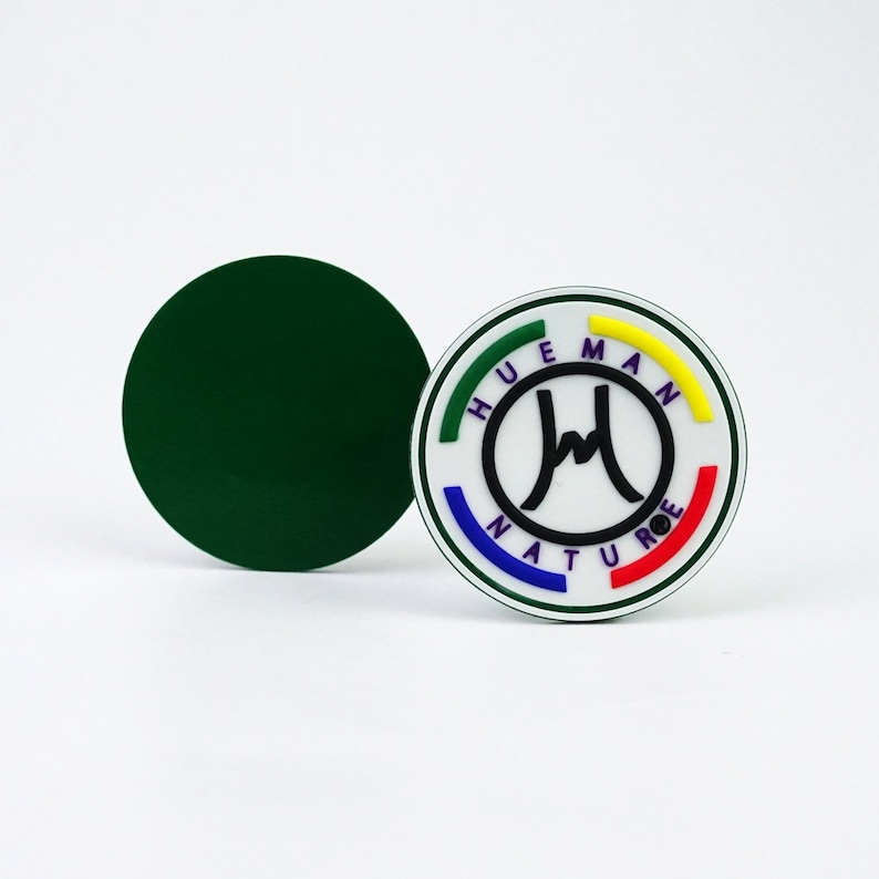 May include: A green circle sticker with a white circle in the center. The white circle has a black logo with the text "HUEMAN NATURE" in a rainbow colored circle around the logo.