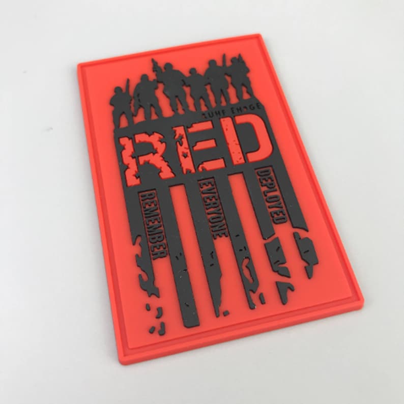 May include: Red, white, and blue American flag patch with the word "RED" in large black letters and the words "Remember Everyone Deployed" in smaller black letters.
