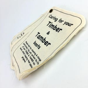 May include: A white fabric tag with black text that reads "Caring for your Timber & Tamber boots. Please read the cleaning & storage instructions. This will extend the life of your Timber & Tamber rain boots, whilst keeping them looking gorgeous."