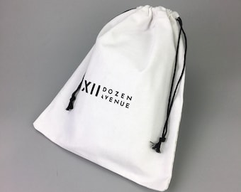 May include: White cotton drawstring bag with black drawstrings and the text "XIII DOZEN AVENUE" printed in black.