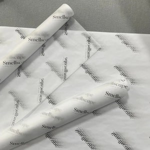 Peut inclure: Papier de soie blanc avec un logo noir répété portant l'inscription Smellscape. Le papier est présenté en deux sections partiellement roulées, affichant une texture fine et semi-translucide avec le nom de la marque imprimé en motif répété.