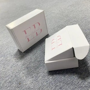May include: Two white cardboard boxes with the logo "Beautyfully LD" printed in pink on the top of each box. The boxes are designed for shipping and have a flap that opens to reveal the inside.