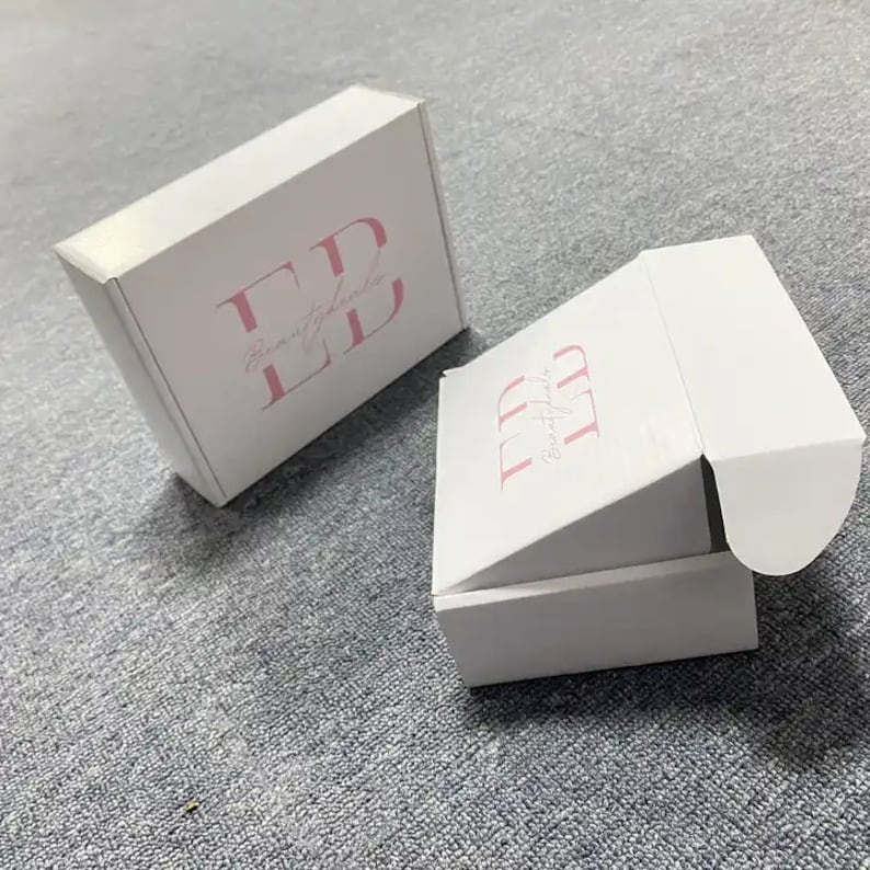 May include: Two white cardboard boxes with the logo "Beautyfully LD" printed in pink on the top of each box. The boxes are designed for shipping and have a flap that opens to reveal the inside.