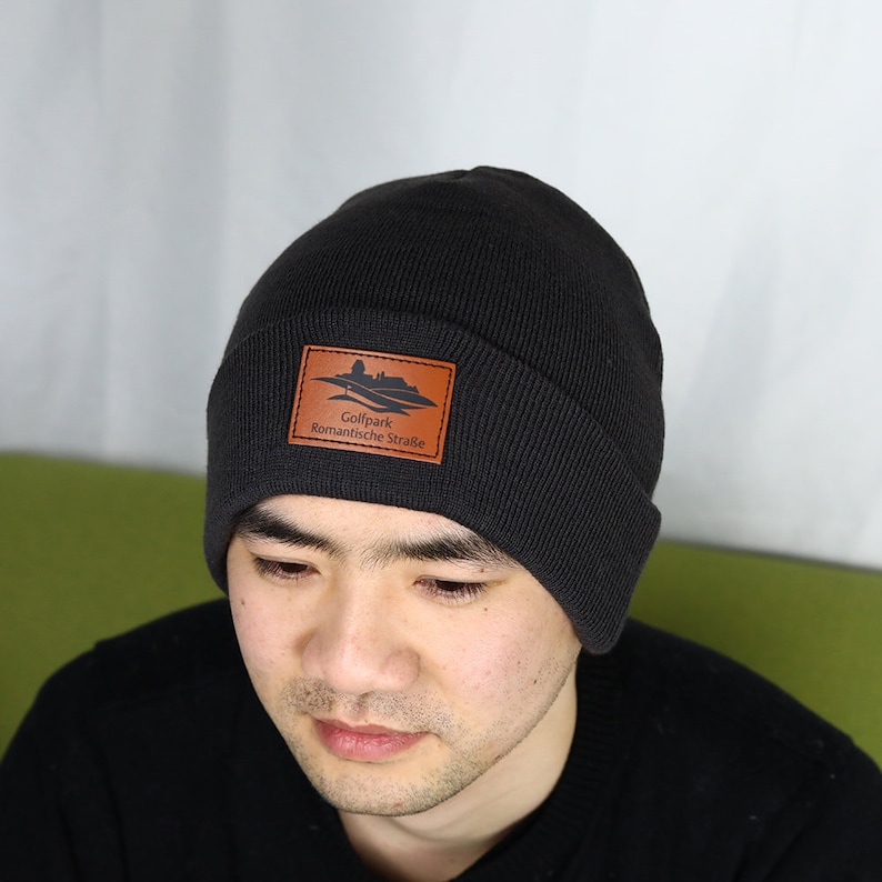 May include: Black knit beanie with a brown leather patch that says "Golfpark Romantische Stra&szlig;e".