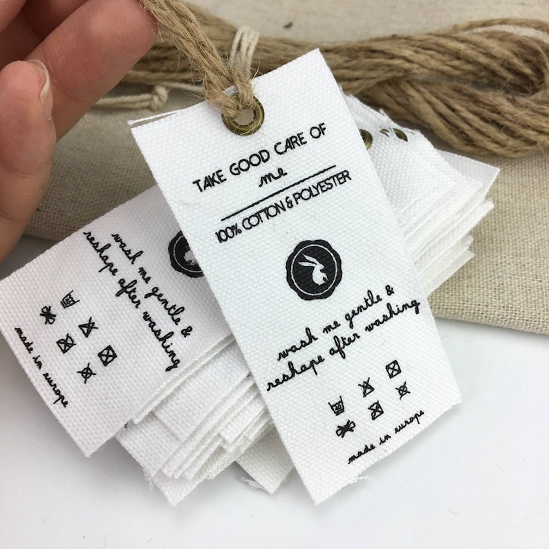 May include: A stack of white cotton and polyester fabric tags with black text and symbols. The tags read "Take good care of me 100% cotton & polyester", "Wash me gentle & reshape after washing", and "Made in Europe".