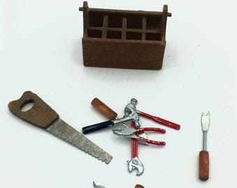 May include: A set of miniature tools, including a saw, hammer, pliers, wrench, screwdriver, and a pry bar, all with wooden handles. The tools are arranged around a small wooden toolbox.