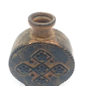 May include: A small, brown ceramic vase with a rounded body and a narrow neck. The vase has a decorative pattern of black and brown diamonds with floral motifs.