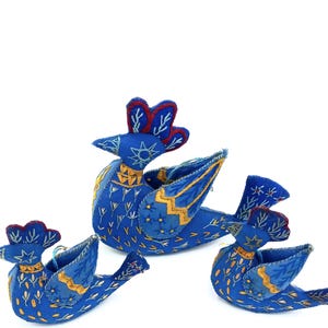 May include: Three blue felt birds with embroidered details. The largest bird has a red crest and a star on its chest. The birds are all facing the right side of the image.