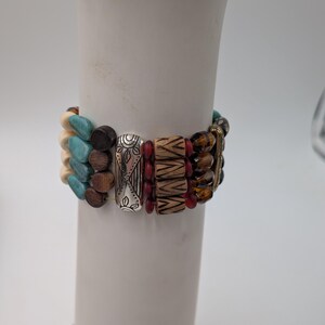 May include: A multi-strand bracelet with a variety of beads in turquoise, brown, cream, and red. The bracelet also features silver-toned metal accents with etched designs. The beads are strung together with elastic.