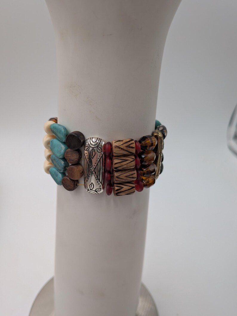 May include: A multi-strand bracelet with a variety of beads in turquoise, brown, cream, and red. The bracelet also features silver-toned metal accents with etched designs. The beads are strung together with elastic.