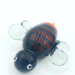 May include: A glass bee figurine with black and orange stripes, clear wings, and black eyes.