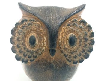 May include: A brown and black ceramic owl figurine with large, round eyes. The owl has a textured surface and a detailed design.