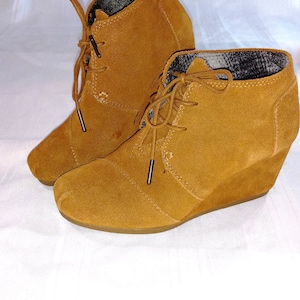 May include: A pair of brown suede wedge ankle boots with lace-up closures. The boots have a brown suede upper and a brown wedge heel.