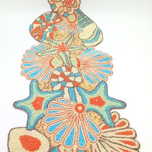May include: A beaded table runner with a seashell design in shades of orange, blue, and green. The runner features a variety of seashells, including starfish, clams, and scallops.