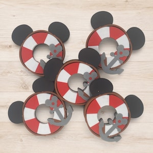 Peut inclure: Quatre ornements circulaires en forme de bouée de sauvetage à rayures rouges et blanches, chacun agrémenté de deux oreilles circulaires noires et d'une ancre grise avec une petite découpe circulaire au sommet, disposés sur un fond en bois clair.