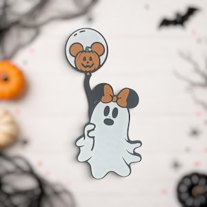 Peut inclure: Une broche émaillée en forme de fantôme blanc avec des yeux et une bouche noirs, portant un nœud marron sur la tête. Le fantôme tient une ficelle reliée à un ballon rond contenant une citrouille orange avec des oreilles de souris et une tige verte.