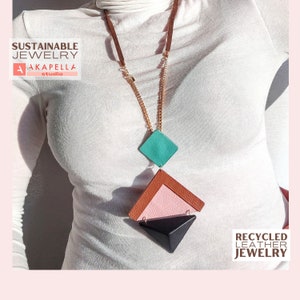 Puede incluir: Un collar geométrico hecho de cuero reciclado. El collar presenta un colgante de cuero turquesa, rosa y negro con una cadena dorada.