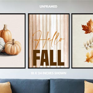 May include: Set of three framed art prints with a fall theme. One print features pumpkins, another says "Hello FALL", and the third shows autumn leaves. The prints are displayed above a blue sofa.