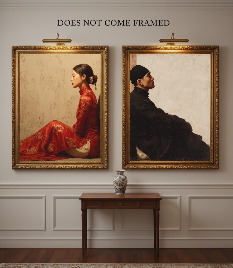May include: Two framed portraits hang on a wall, each with a gold frame and a warm-toned image. One depicts a person in a red dress, the other a person in black clothing. A small wooden table and a decorative vase are below the portraits. Text above the frames reads "DOES NOT COME FRAMED."