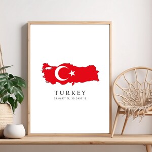 May include: A white framed print with a red outline of Turkey with the Turkish flag inside. The text "TURKEY" is below the map with the coordinates "38.9647° N, 35.2433° E".