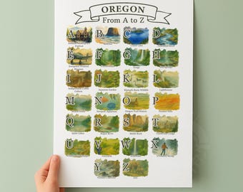 May include: A poster titled "Oregon From A to Z" features watercolor illustrations of Oregon landmarks, each labeled with a letter of the alphabet. The poster is held by a person's hand. The poster is white with black text and colorful images.