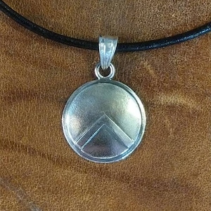 Può includere: Collana con ciondolo in argento a forma di scudo rotondo con un motivo a chevron stilizzato. Il ciondolo è su un cordoncino in pelle nera.